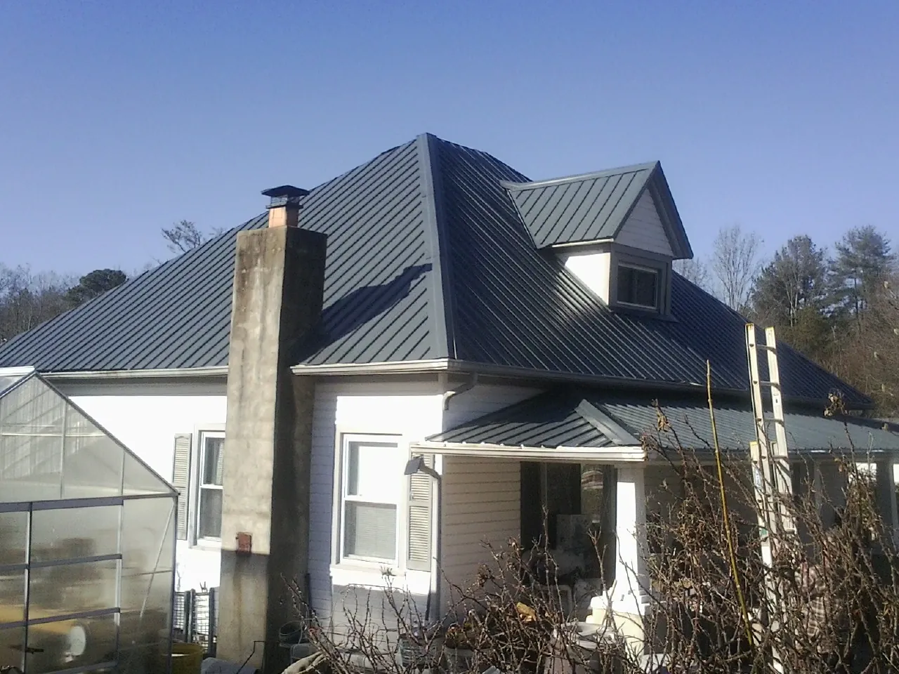 Dark blue standing seam metal roof on a white farmhouse with dormer — Slate & Tile Roof Repair by Roofing Brothers in Gautier
