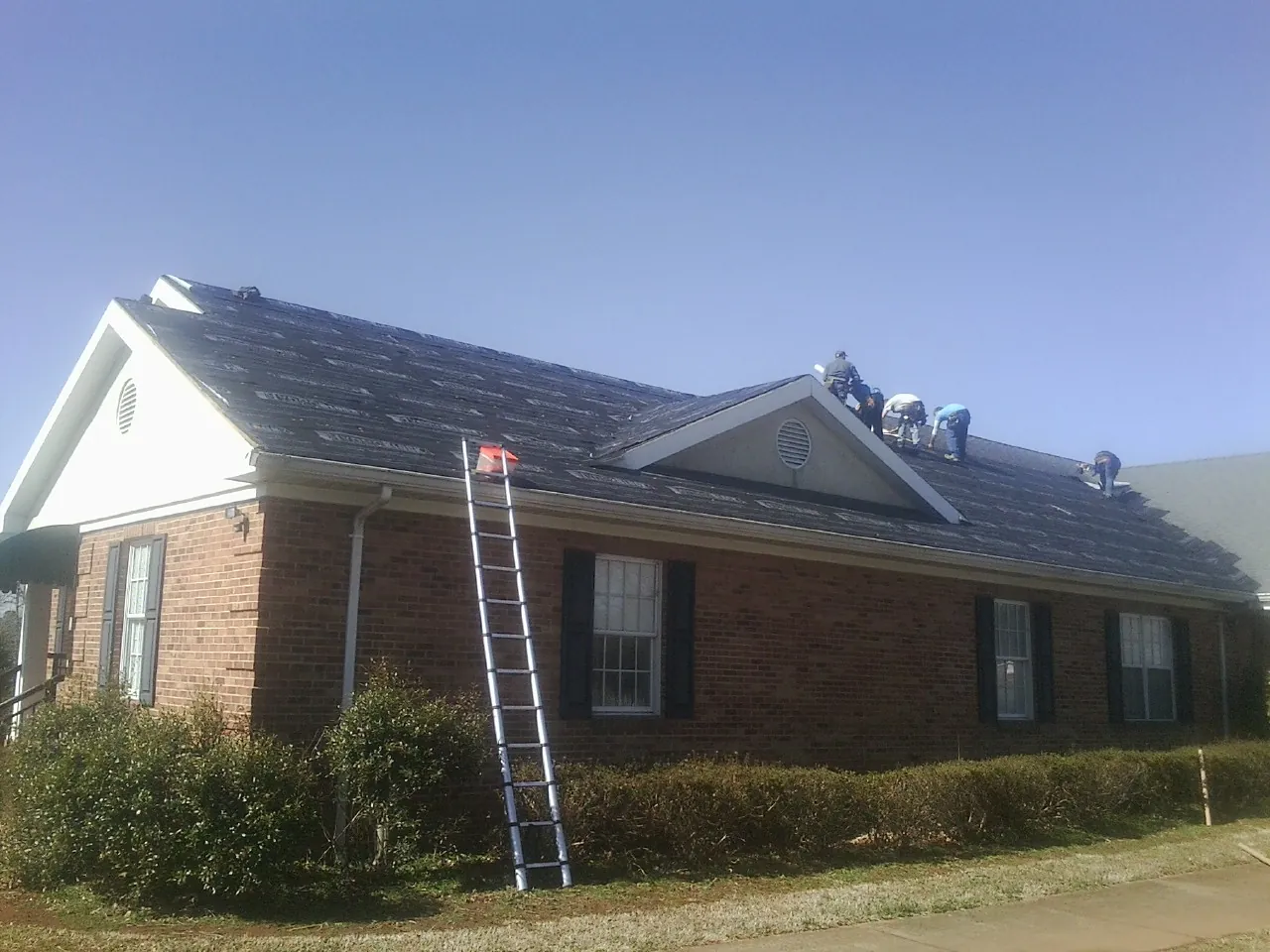 Crew tearing shingles off a brick ranch roof with a ladder set — Emergency Roof Repair work by our crew in Gautier