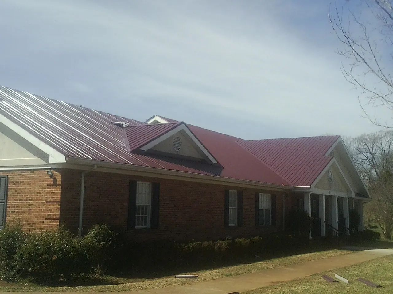 Red metal roof with gabled entries on a long brick building, from a Hail Damage Roof Repair job in Gautier