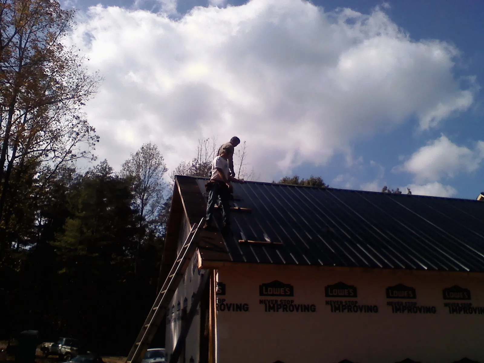 Roofer fastening dark metal panels high against a cloudy sky, from a Roof Inspection job in Gautier