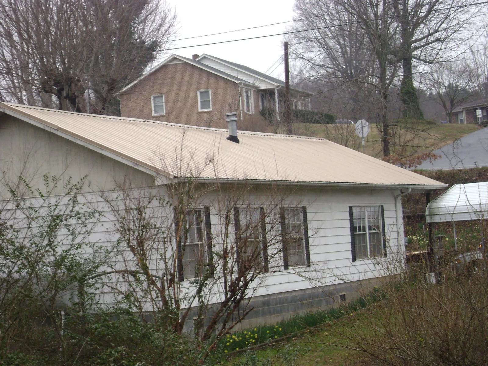 Tan metal roof on a white sided house set into a hillside — Commercial Roofing by Roofing Brothers in Gautier