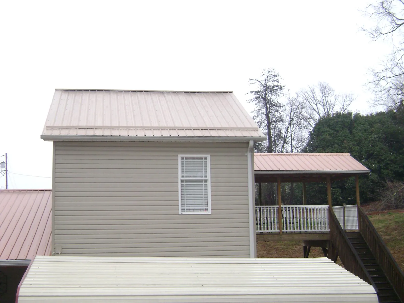 Tan metal roofs on a two story addition and attached porch, from a Roof Replacement job in Gautier